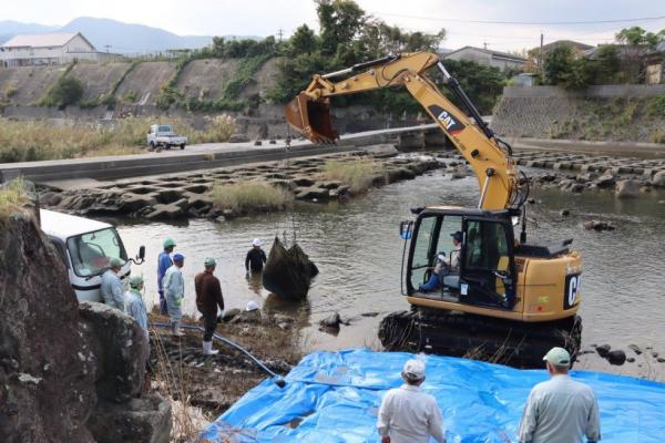 川に沈んだ石倉カゴを重機で引き上げる様子