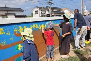 黄色い塗料で手形を押している子どもたちと河野さんの後ろ姿の写真