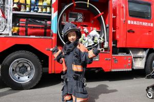 消防車の前で消防の装備を着てポーズをとっている子どもの写真
