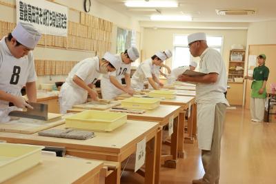 そば打ちをしている受験者と審査している師範代の写真