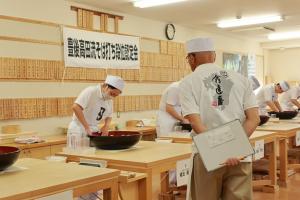 受験者とそば打ちの様子を間近で見ている審査委員長の写真