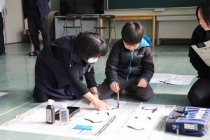 地域の方に教えてもらいながら字を書いている児童の写真
