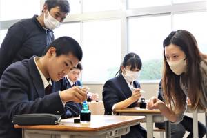 ガラスペンで字を書く生徒と、見つめるワンチャーの社員