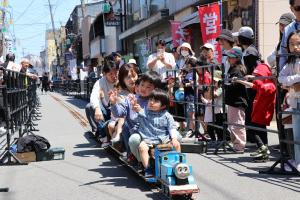 昭和の町商店街を走るミニ鉄道とその様子を見守るお客さんの様子