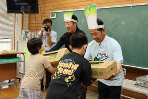 白ねぎ生産者から児童へ白ねぎを贈呈する様子