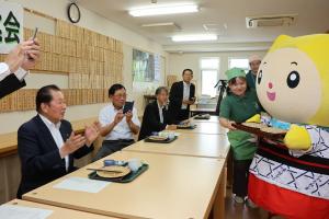おかわりのそばを運んでいるそばみちゃんと見守っている参加者たちの写真