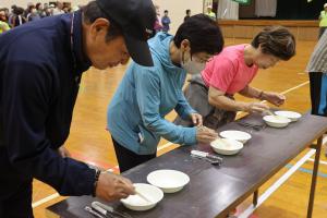 碁石を箸やスプーンで掴んで隣の皿に移す様子