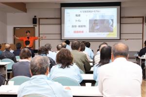 防災アトラクションで解説している講師と説明を聞く防災士たちの写真