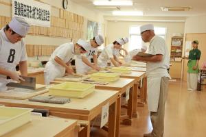 そば打ちをしている受験者と審査している師範代の写真