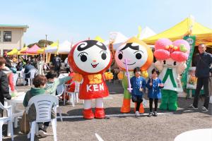 屋外の販売コーナーを背景とした3体のキャラクター